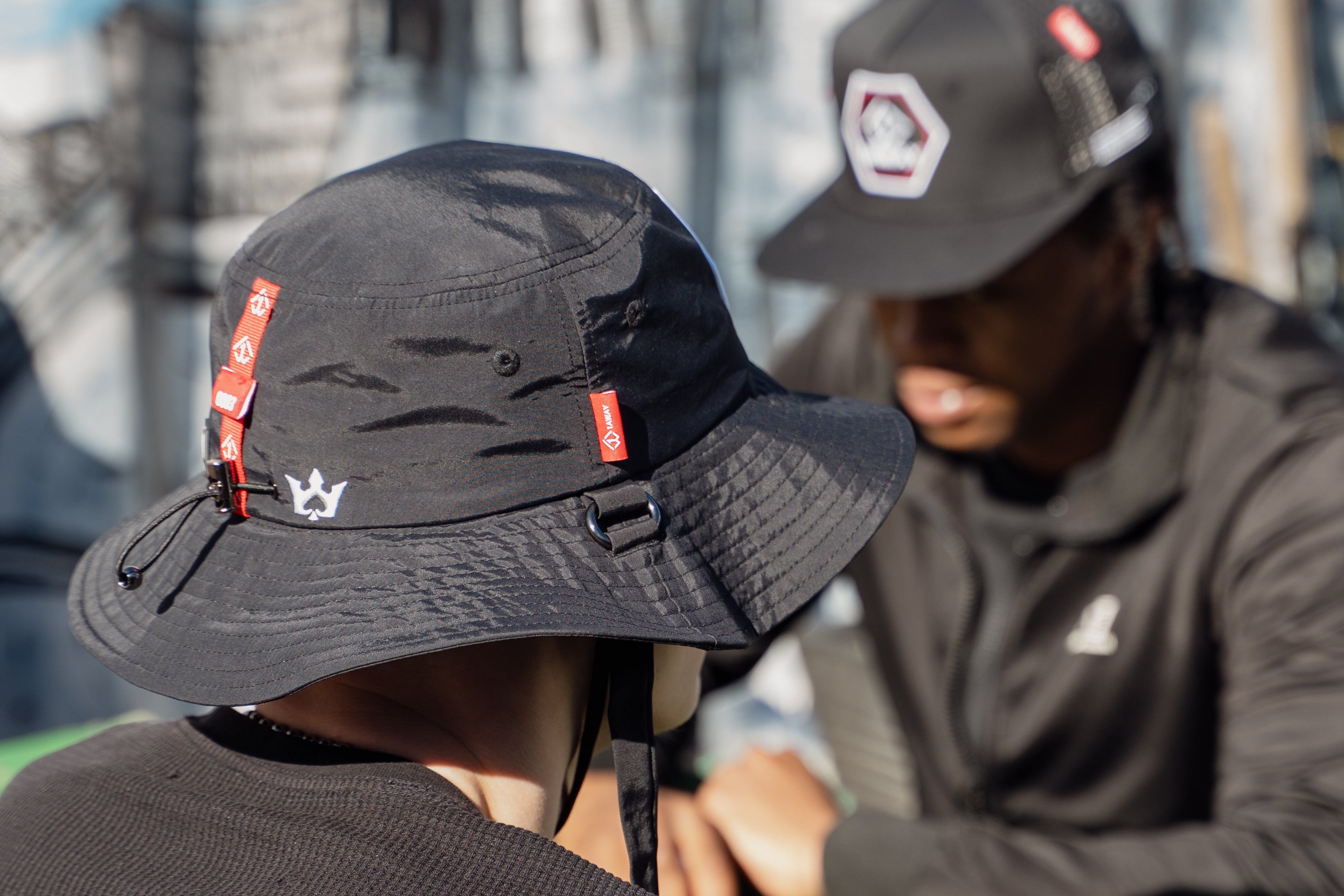 Person wearing a black 1AWAY bucket hat with red accents and a logo, sitting outdoors.