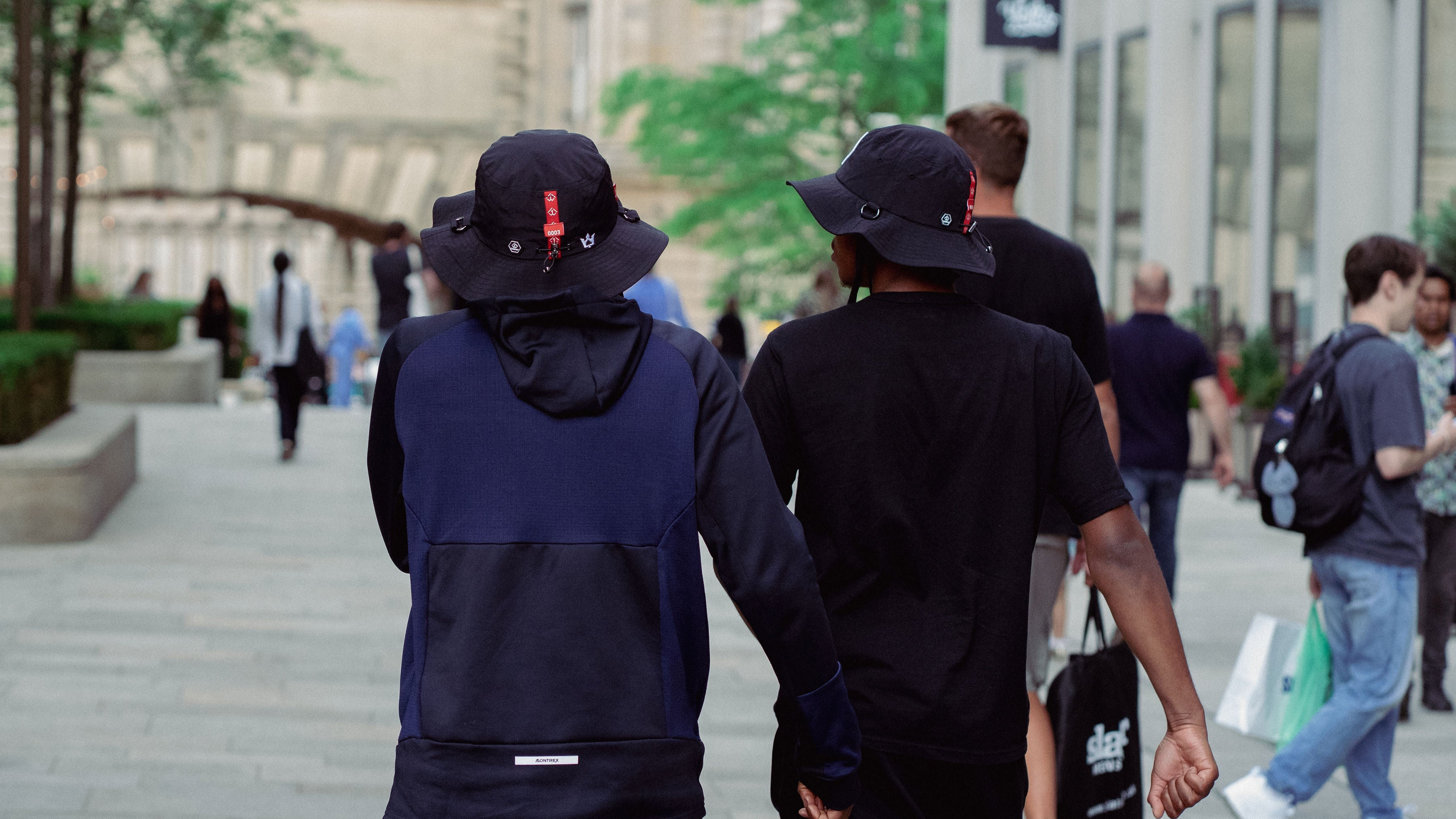 Two individuals walking together on a city street, wearing black hats and dark clothing.