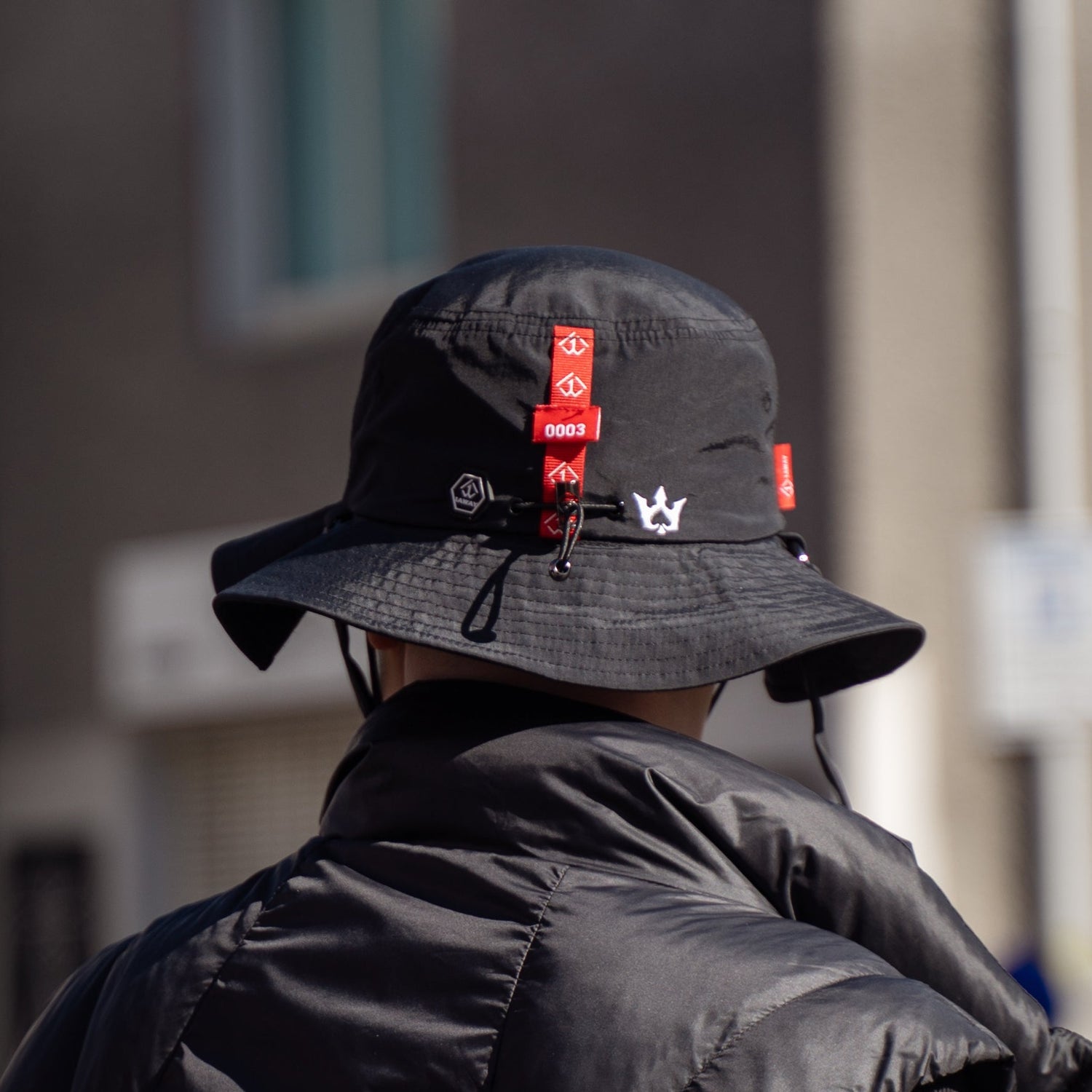black 1AWAY 0003 bucket hat with red accents and a black jacket in an urban setting.
